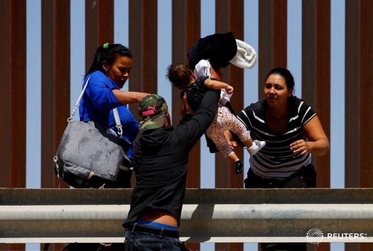 An asylum-seeking migrant hands a child over a railing after crossing the Rio Br