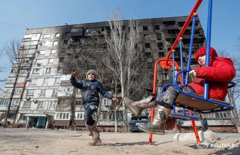 Children play in front of a building damaged in fighting during Russia’s invasio