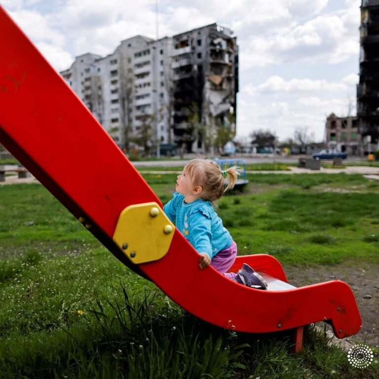 Nina Stefuryak, 2, plays on a playground in front of a building destroyed by she