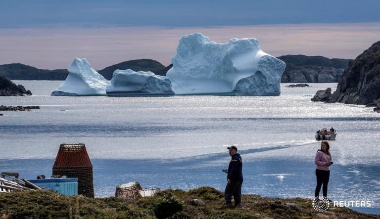 Visitors watch as a large iceberg drifts off the coast of Merritt’s Harbour in N